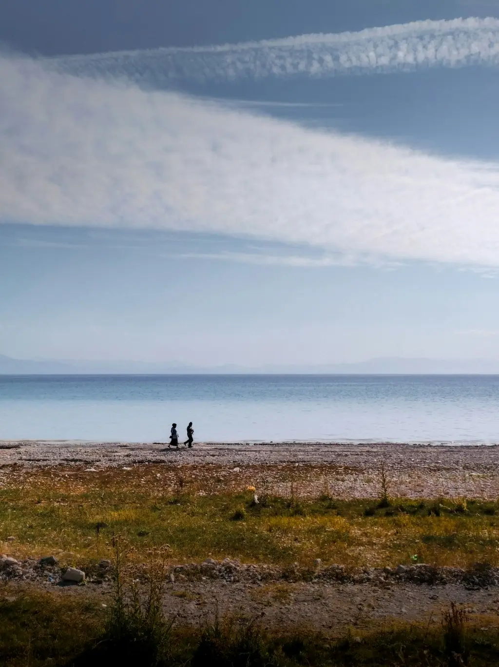 A couple walking by the lake. Cloudy blue sky in the background.